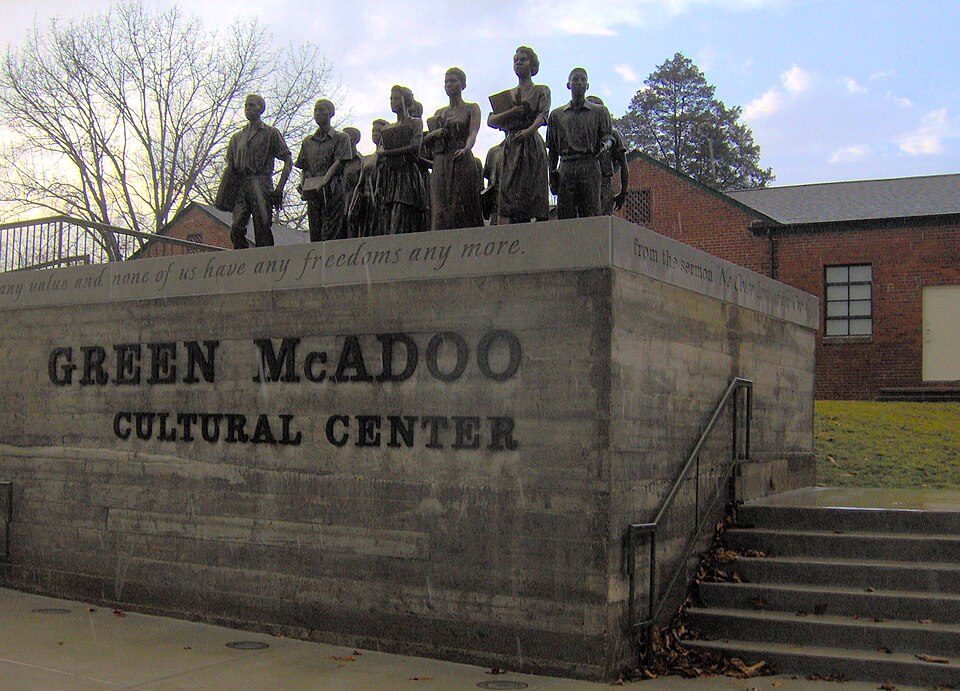 The Green McAdoo Cultural Center sign wall in Clinton, Tennessee, topped by a bronze sculpture of students carrying books