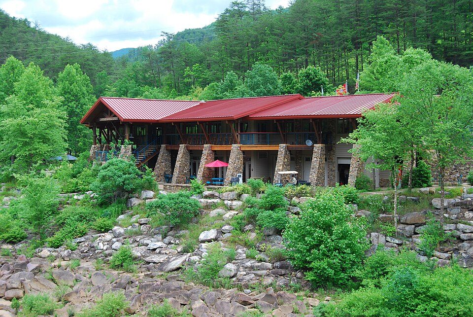 The former Ocoee Whitewater Center, a red-roofed building on stone piers above the rocky Ocoee River course, before it was destroyed by fire in 2022